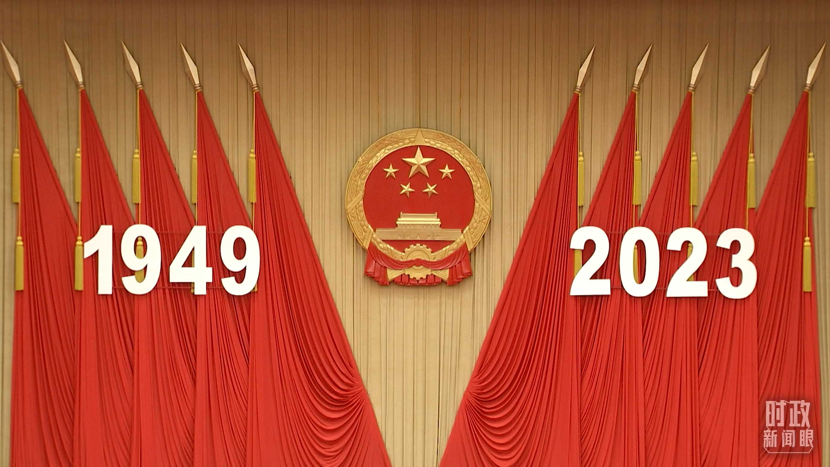 △人民大会堂宴会厅内，主席台上方高悬着庄严的国徽，“1949－2023”大字年号在鲜艳的红旗映衬下格外醒目。