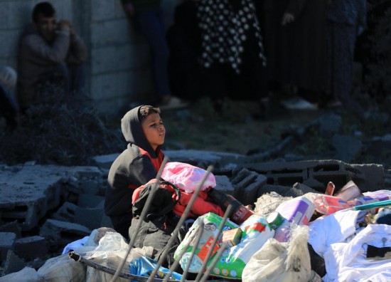 1月7日，在加沙地带南部城市拉法，一名男孩坐在以军空袭后的废墟旁。新华社发（亚西尔·库迪摄）