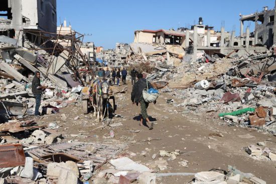 1月7日，人们走过加沙城的建筑废墟。新华社发（穆罕默德·阿里摄）