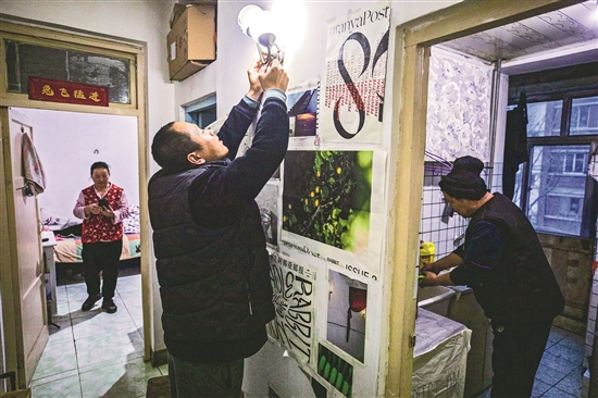 1月17日，北京市门头沟区军庄镇，高新强（图中）正在新租住的单元房里更换灯泡。水害发生后，他们在镇上租了一套单元房，等今年开了春再对受损房屋进行整修。