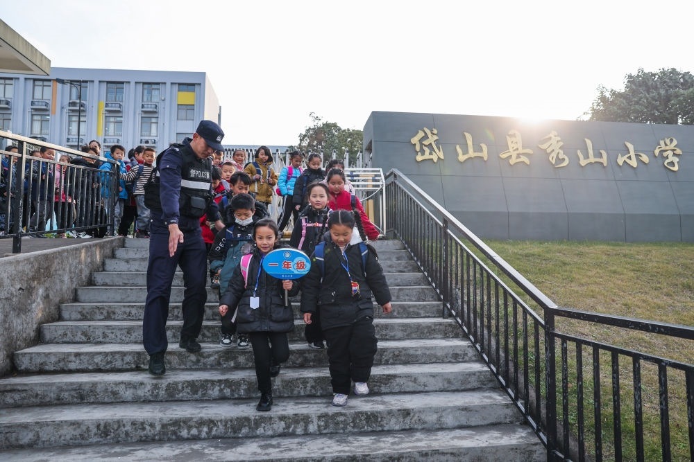 2023年12月20日，秀山派出所民警在秀山小学放学时间参与“护学岗”维持秩序，同时接独自放学的学生去“民生小铺”。浙江省舟山市岱山县公安局秀山派出所联合乡镇、社区成立“民生小铺”，为当地居民、外来务工人员及其子女等服务，协助解决外来务工人员在工作、生活等方面的矛盾和问题，助力乡镇基层治理。新华社记者 徐昱 摄